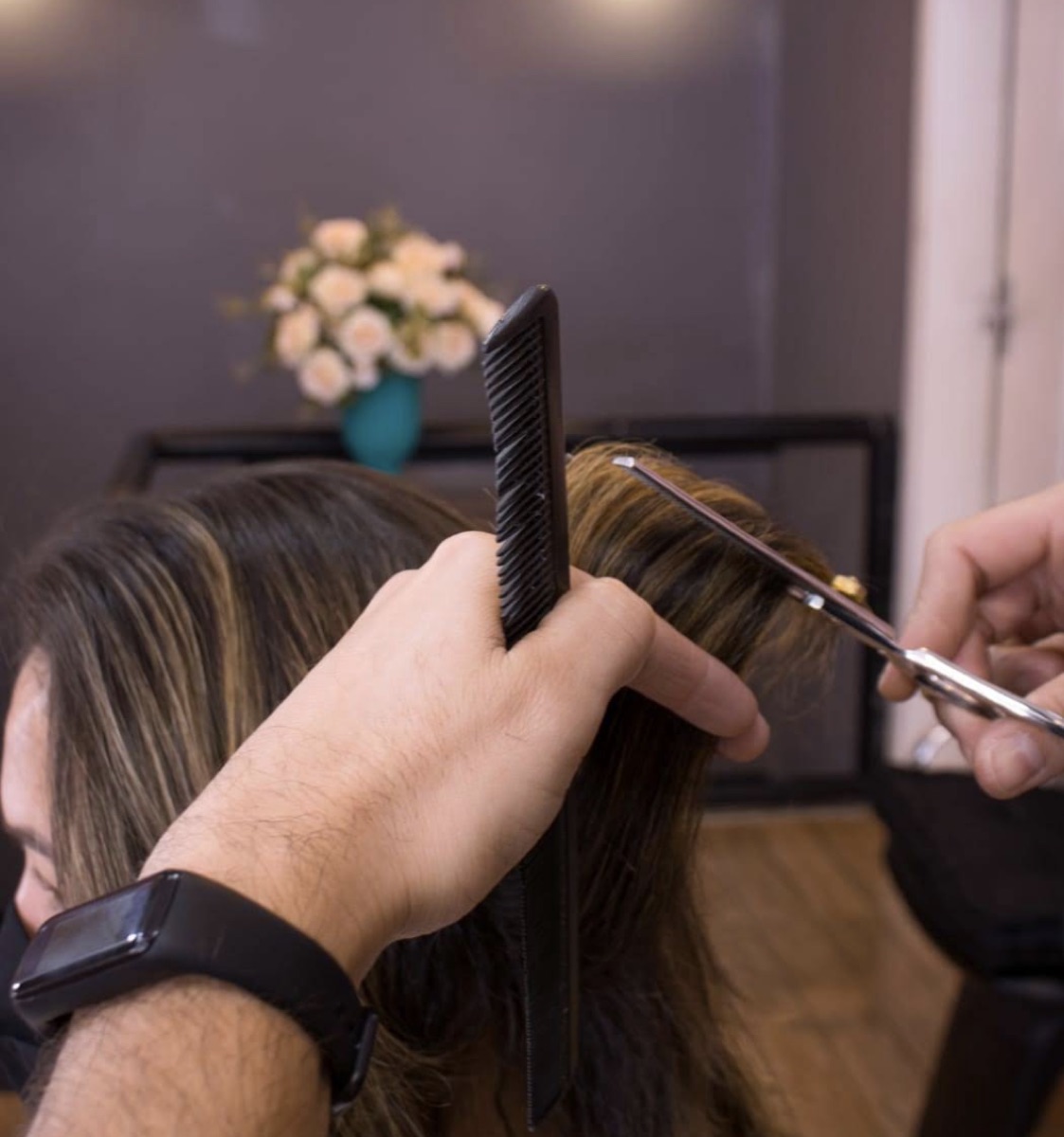 Detalhe das mãos de Diego Moreira cortando cabelo com pente e tesoura