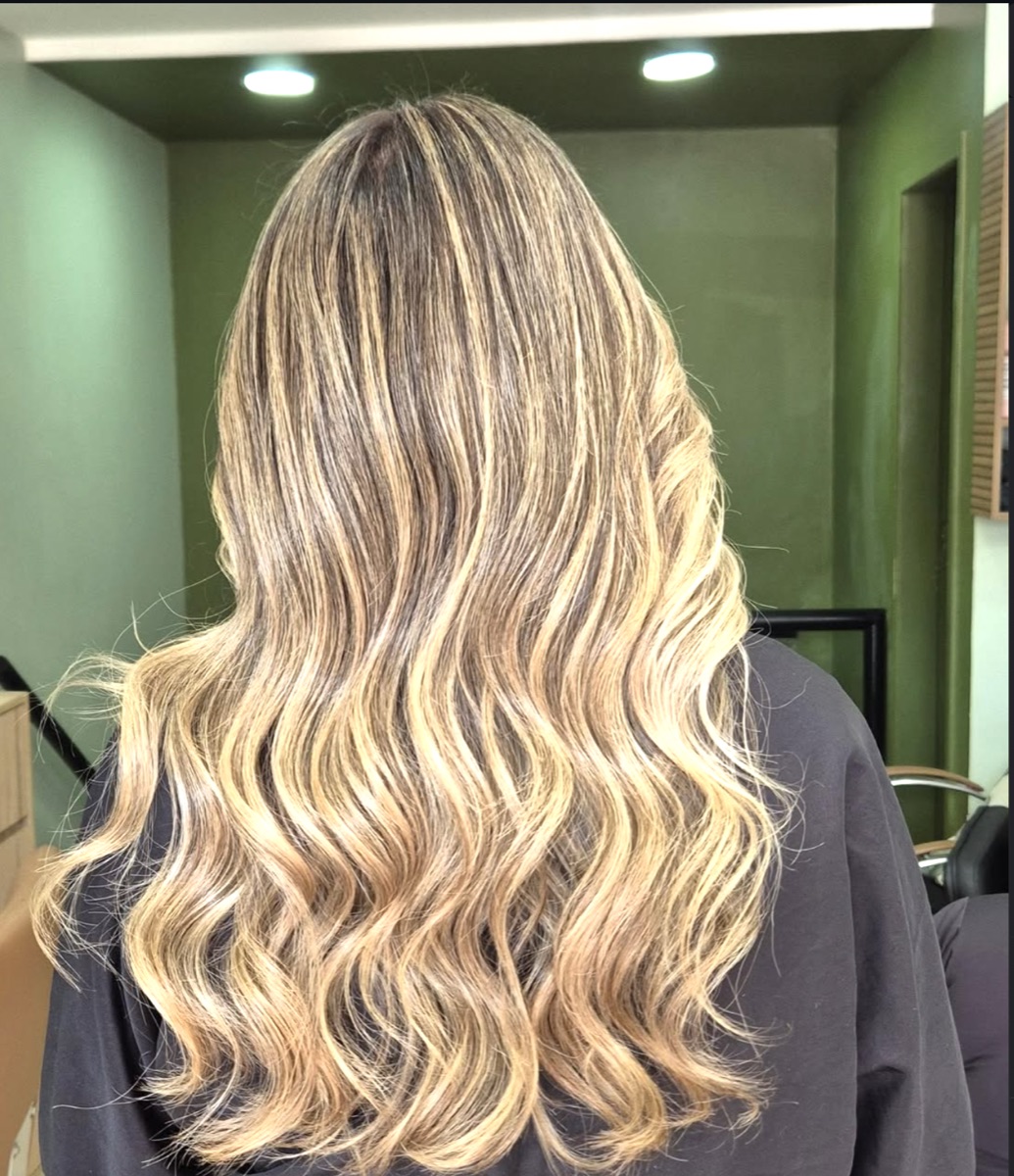 Cabelo longo com balayage loiro e raiz esmaecida, vista de costas, no salão