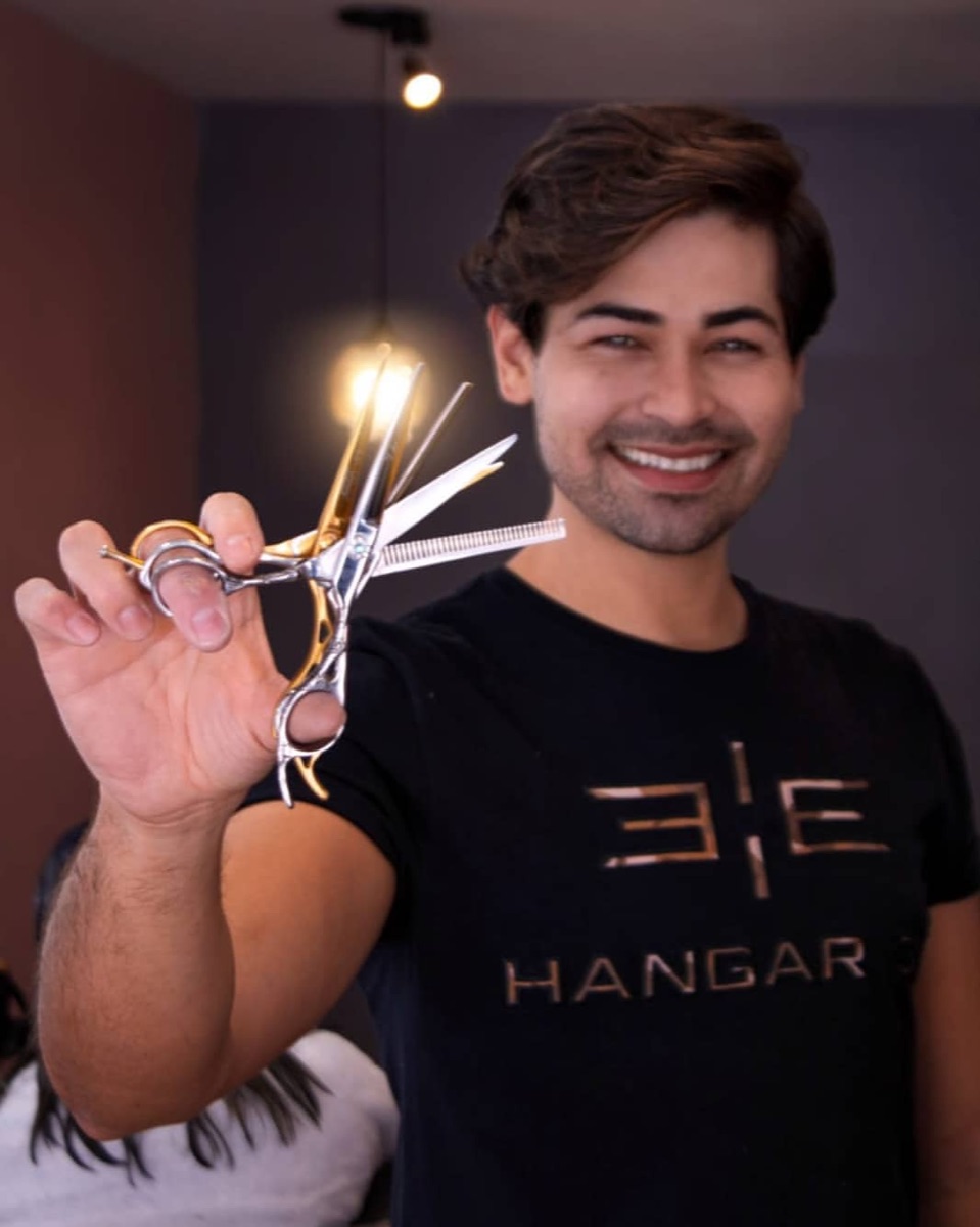 Diego Moreira segurando tesoura de corte, sorrindo, em atendimento no salão