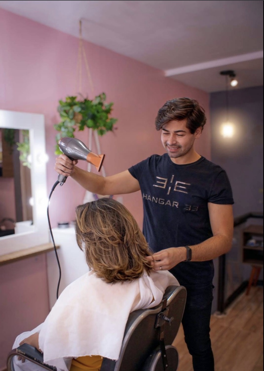 Diego Moreira finalizando escova modelada em cliente, sorrindo, no salão